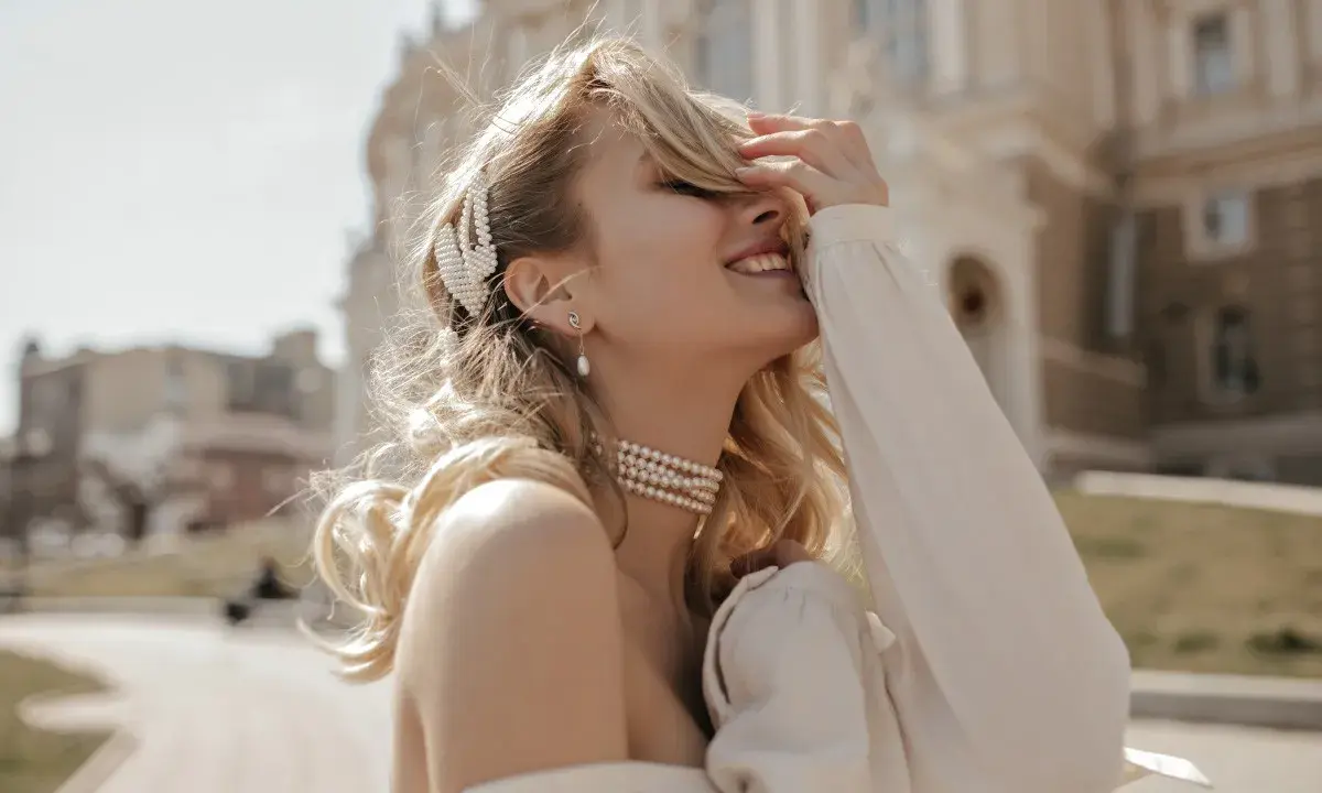 Uśmiechnięta blondynka w perłowej biżuterii, z perłową spinką we włosach. Masa perłowa znaczenie symbolizuje czystość i piękno.