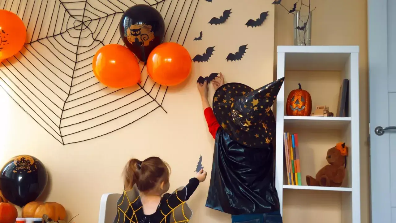Dzieci w strojach na Halloween dekorują pokój, wieszając nietoperze na ścianie z wielką pajęczyną.