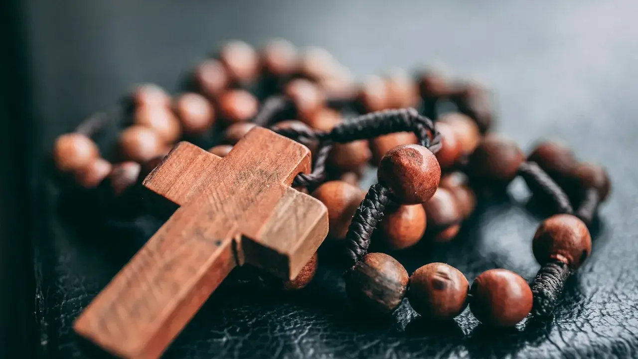 Drewniany krzyż i paciorki różańca, symbol wiary i modlitwy. Jeden dziesiątek różańca leży na ciemnym tle.