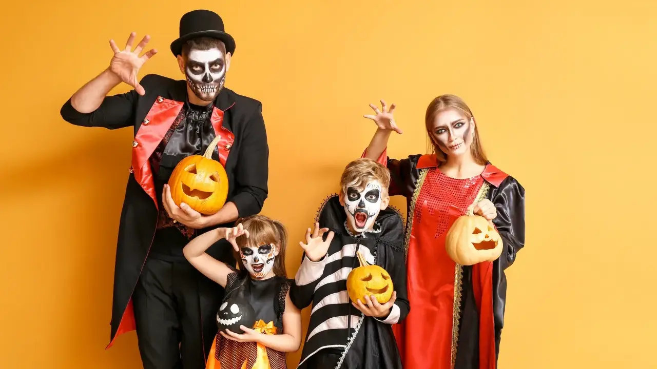 Rodzina w strojach na Halloween z dyniami i makijażem czaszki na żółtym tle.