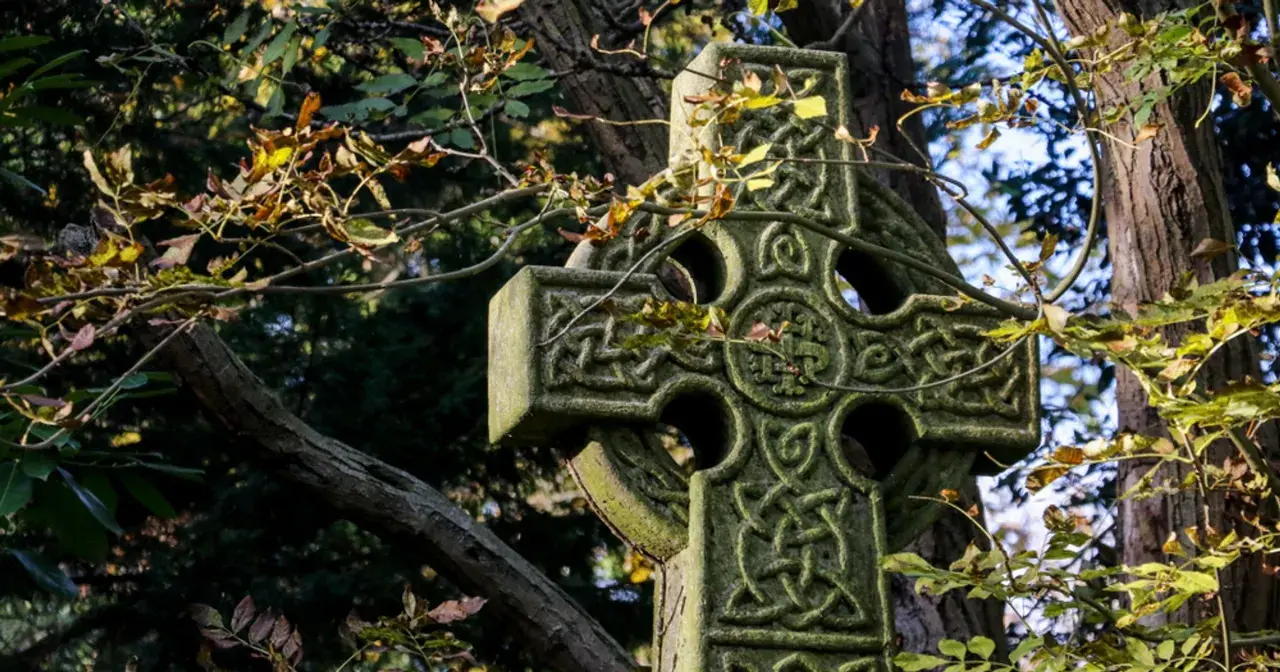 Kamienny krzyż celtycki z misternymi wzorami, otoczony jesiennymi liśćmi. Jego znaczenie symbolizuje wieczność i połączenie.