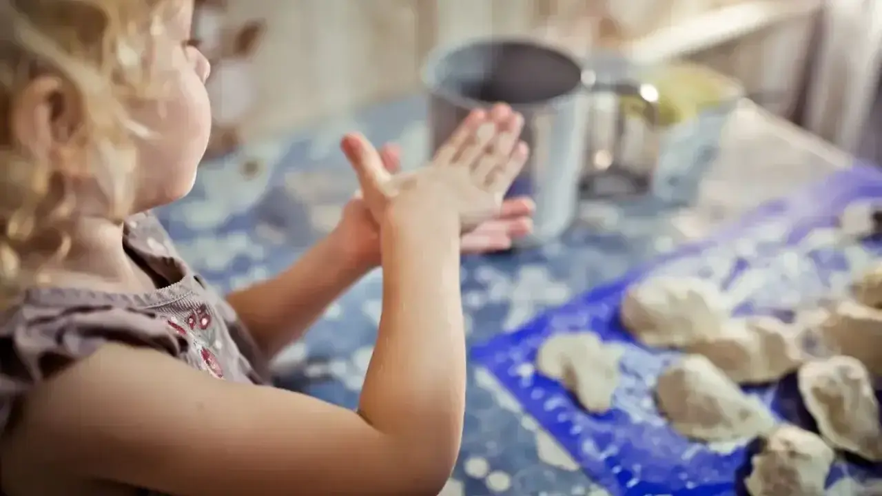 Mała dziewczynka z kręconymi włosami tworzy coś z masy plastycznej. To świetne kreatywne zabawy z 6 latkiem, rozwijające wyobraźnię i zdolności manualne.