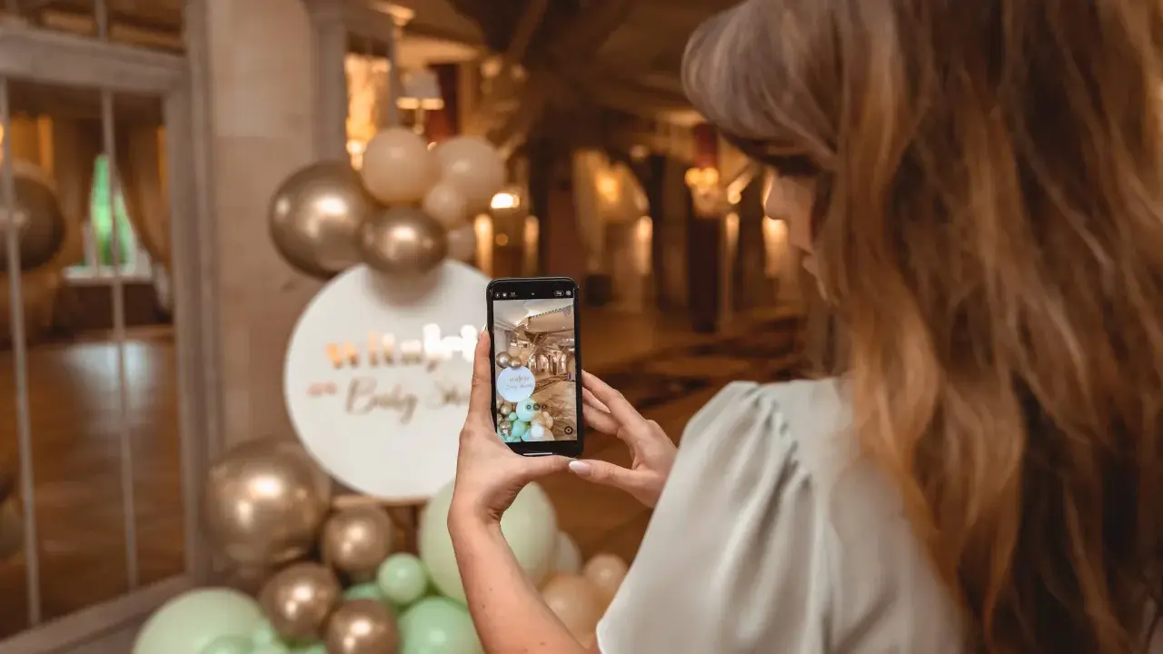 Kobieta robi zdjęcie dekoracji na baby shower. Złote i miętowe balony tworzą łuk. Świetne baby shower pomysły!