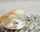 Piękna muszla skrywa perłę, a wokół rozsypane są inne rodzaje pereł naturalnych na piaszczystym tle.