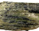 Szarozielony, włóknisty minerał z czarnymi wtrąceniami, przykład rzadkich minerałów.
