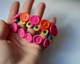 Kolorowa biżuteria z recyklingu z guzików i kapsli na dłoni.