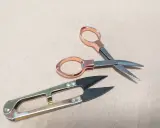 Dwa rodzaje nożyczek, w tym małe nożyczki z miedzianymi uchwytami i większe, metalowe, to niezbędne narzędzia i przybory krawieckie do precyzyjnych cięć.