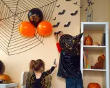 Dzieci w strojach na Halloween dekorują pokój, wieszając nietoperze na ścianie z wielką pajęczyną.