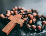 Drewniany krzyż i paciorki różańca, symbol wiary i modlitwy. Jeden dziesiątek różańca leży na ciemnym tle.