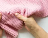 Dłonie trzymają różowy sweter z dziurą, pokazując problem, jak zaszyć dziurę w dresach.