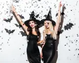 Dwie kobiety w czarnych sukienkach i kapeluszach czarownic, otoczone nietoperzami i konfetti, to świetny pomysł na kostium halloween.