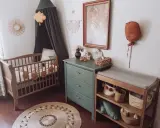 Przytulny pokój dziecka boho z drewnianym łóżeczkiem, przewijakiem i zieloną komodą. Dekoracje w stylu boho tworzą ciepłą atmosferę.