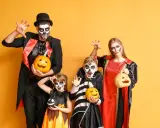 Rodzina w strojach na Halloween z dyniami i makijażem czaszki na żółtym tle.