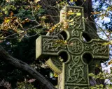 Kamienny krzyż celtycki z misternymi wzorami, otoczony jesiennymi liśćmi. Jego znaczenie symbolizuje wieczność i połączenie.
