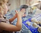 Mała dziewczynka z kręconymi włosami tworzy coś z masy plastycznej. To świetne kreatywne zabawy z 6 latkiem, rozwijające wyobraźnię i zdolności manualne.
