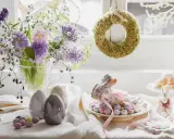 Wielkanocne dekoracje: bukiet wiosennych kwiatów, ceramiczne jajka, lukrowany zajączek otoczony cukierkami i mechowy wianek.