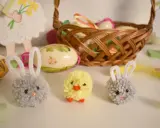 Urocze ozdoby wielkanocne z recyklingu: puchate zajączki i kurczaczek. W tle koszyk z pisankami i wielkanocne dekoracje.