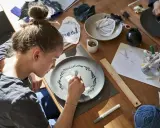 Dziewczyna maluje na talerzu, tworząc wzór. Wokół materiały do rękodzieła, jak do zimna porcelana przepis.