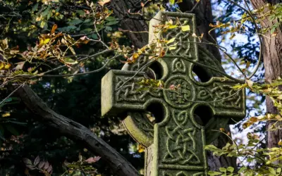 Kamienny krzyż celtycki z misternymi wzorami, otoczony jesiennymi liśćmi. Jego znaczenie symbolizuje wieczność i połączenie.