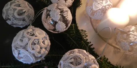Ozdoby choinkowe z białej koronki na gałązkach jodły, obok świec.