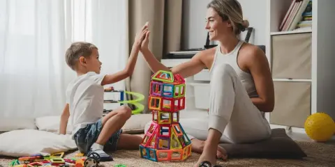 Mama i syn świętują sukces kreatywnych zabaw plastycznych, budując wieżę z kolorowych klocków.