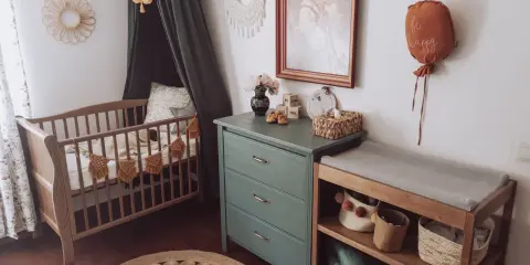 Przytulny pokój dziecka boho z drewnianym łóżeczkiem, przewijakiem i zieloną komodą. Dekoracje w stylu boho tworzą ciepłą atmosferę.