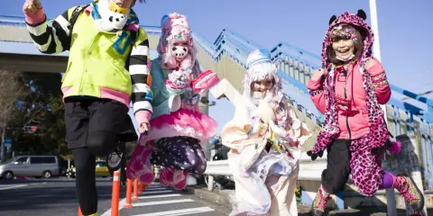 Japoński projektant mody inspiruje się stylem Harajuku. Cztery osoby w kolorowych, ekstrawaganckich strojach pozują na tle niebieskich schodów.