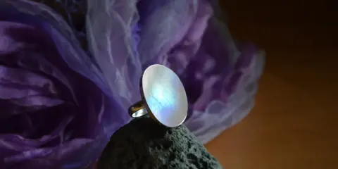 Pierścionek z kamieniem księżycowym, którego magiczne właściwości przyciągają wzrok. Opalizujący kamień lśni na tle fioletowej tkaniny.