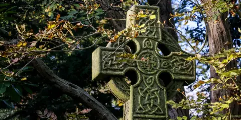 Kamienny krzyż celtycki z misternymi wzorami, otoczony jesiennymi liśćmi. Jego znaczenie symbolizuje wieczność i połączenie.