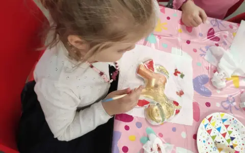 Dziewczynka maluje złotą farbą gipsową figurkę renifera.