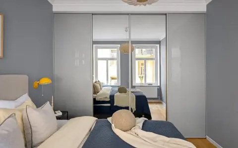 Szafa z drzwiami przesuwnymi w kolorze platyna odbija łóżko i okna.