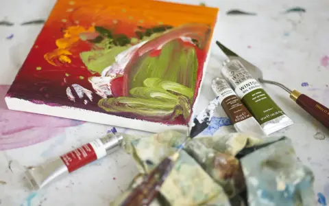 Płótno z barwnym obrazem, tubki farb olejnych Winsor & Newton, paleta i pędzle – idealne narzędzia, by dowiedzieć się, jakimi farbami malować na płótnie.