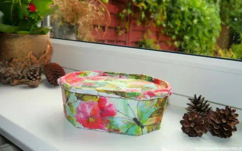 Uroczy koszyczek z motywem kwiatów i motyli, wykonany techniką decoupage na plastiku. Idealny do przechowywania drobiazgów.