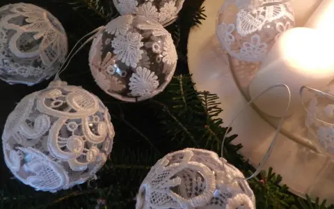 Ozdoby choinkowe z białej koronki na gałązkach jodły, obok świec.