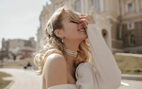 Uśmiechnięta blondynka w perłowej biżuterii, z perłową spinką we włosach. Masa perłowa znaczenie symbolizuje czystość i piękno.