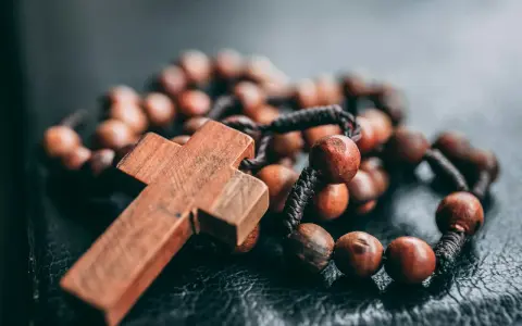 Drewniany krzyż i paciorki różańca, symbol wiary i modlitwy. Jeden dziesiątek różańca leży na ciemnym tle.
