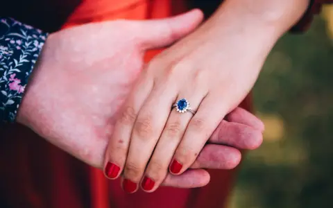 Dłoń z pierścionkiem z szafirem i diamentami, symbol miłości, jak szmaragd i szafir, w dłoniach pary.