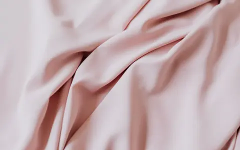 Delikatne fałdy pudrowego sztucznego jedwabiu tworzą miękkie cienie i światła, sugerując elegancję i lekkość.