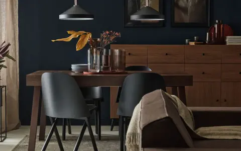 Elegancka jadalnia w odcieniach czarnego i brązu. Czarne krzesła, drewniana komoda i dywan tworzą przytulną atmosferę.