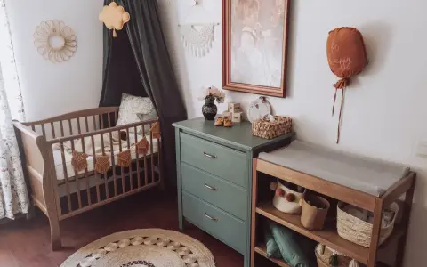 Przytulny pokój dziecka boho z drewnianym łóżeczkiem, przewijakiem i zieloną komodą. Dekoracje w stylu boho tworzą ciepłą atmosferę.