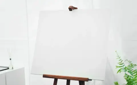 Puste białe płótno na sztalugach, z zieloną rośliną po prawej.