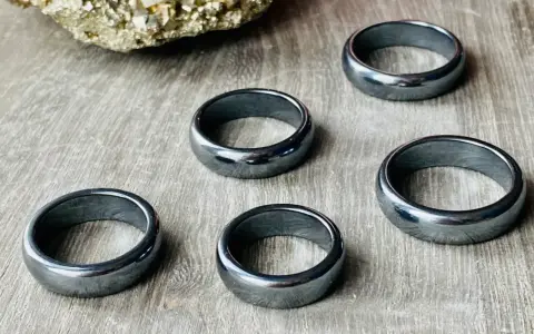 Pięć błyszczących, ciemnoszarych pierścionków z hematytu na drewnianym tle. Jak rozpoznać hematyt? Po jego metalicznym połysku i ciężarze.