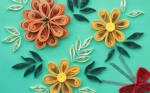 Kwiaty z papieru wykonane techniką quilling dla początkujących. Pomarańczowe, żółte i czerwone kwiaty oraz zielone i białe listki na turkusowym tle.