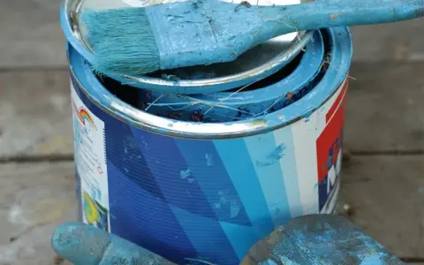 Puszka z niebieską farbą plakatową, pędzel i rękawica pokryte farbą.