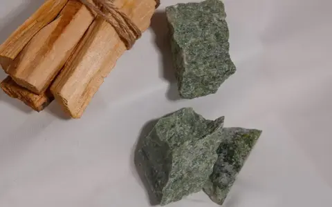 Surowe kawałki jadeitu w odcieniach zieleni, obok wiązki drewna palo santo.