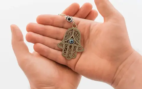 Dłonie trzymające ozdobny amulet w kształcie ręki Fatimy z niebieskim okiem.