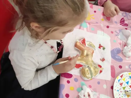 Dziewczynka maluje złotą farbą gipsową figurkę renifera.