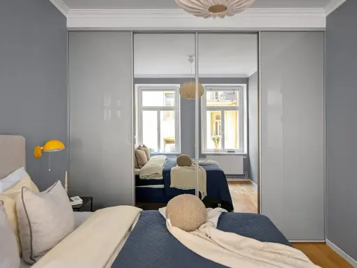 Szafa z drzwiami przesuwnymi w kolorze platyna odbija łóżko i okna.