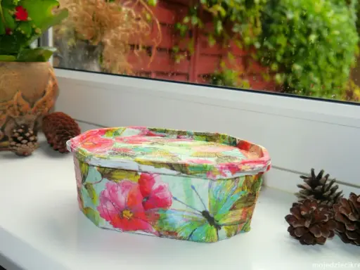 Uroczy koszyczek z motywem kwiatów i motyli, wykonany techniką decoupage na plastiku. Idealny do przechowywania drobiazgów.