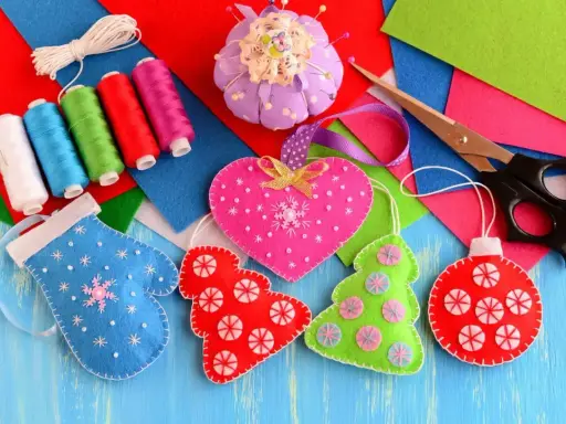 Kolorowe filcowe ozdoby, nici, nożyczki i poduszeczka na szpilki.